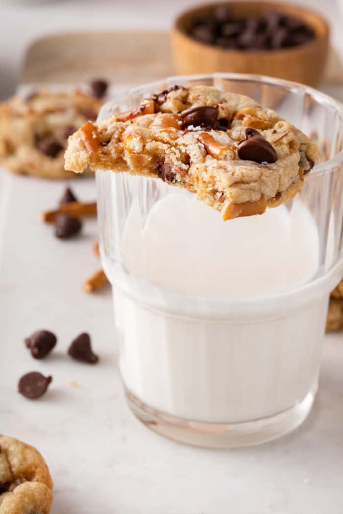 Kitchen sink cookie with a bite taken from it perched on the edge of a glass of milk.