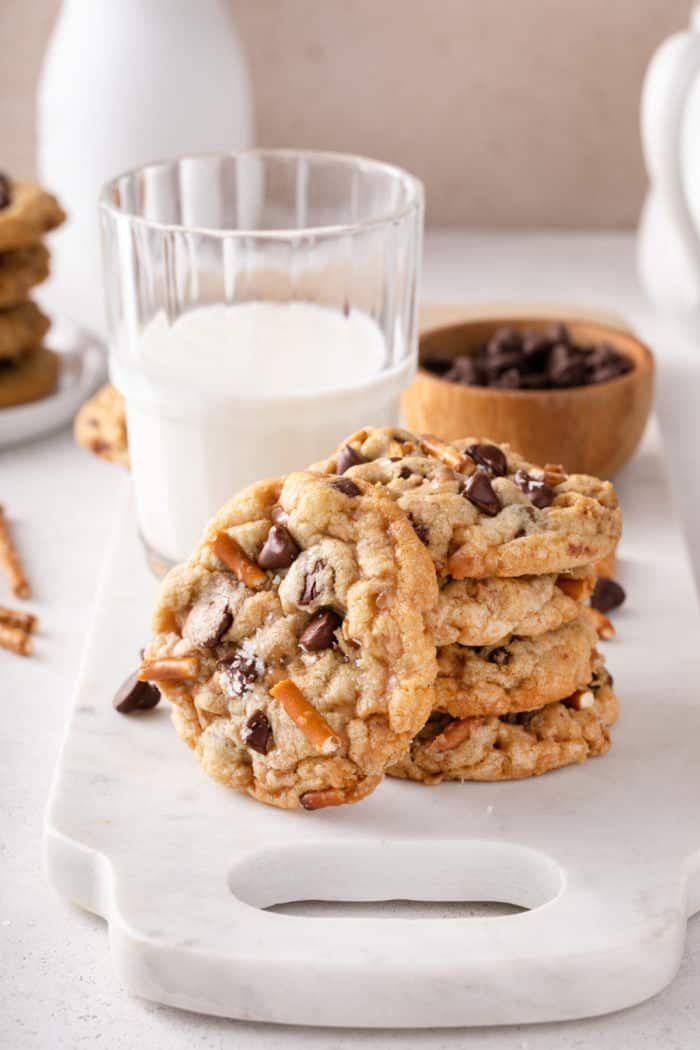 Three kitchen sink cookies stacked in front of a glass of milk. A fourth cookie is leaning against the stack.