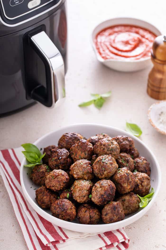 Bowl of air fryer meatballs on a countertop in front of an air fryer.