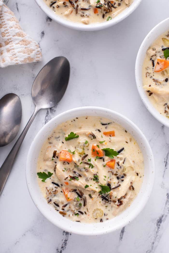 Overhead shot of a bowl of chicken and wild rice soup on a marble countertop, set next to two spoons.