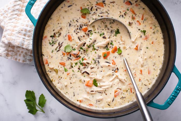 Overhead shot of a blue dutch oven filled with chicken and wild rice soup, being stirred by a ladle.