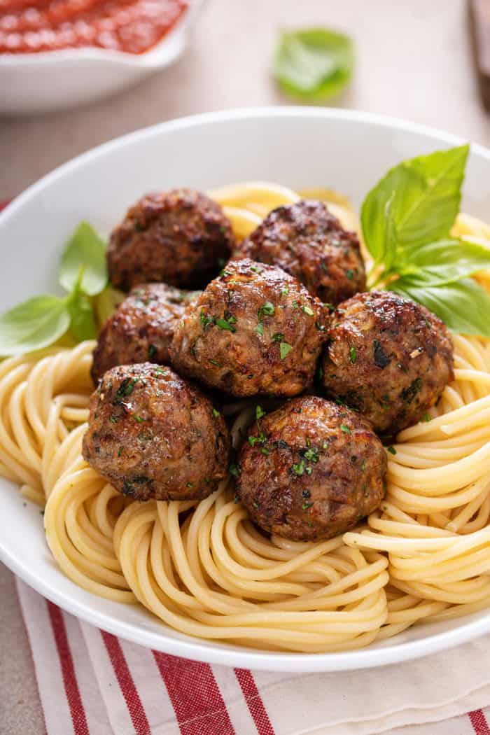 Close up of several air fryer meatballs set on top of a bed of spaghetti.