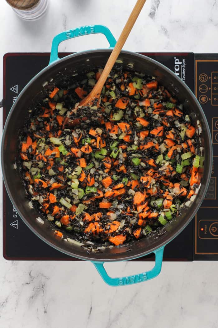 Cooked vegetables and wild rice being stirred together with a wooden spoon in a large dutch oven.