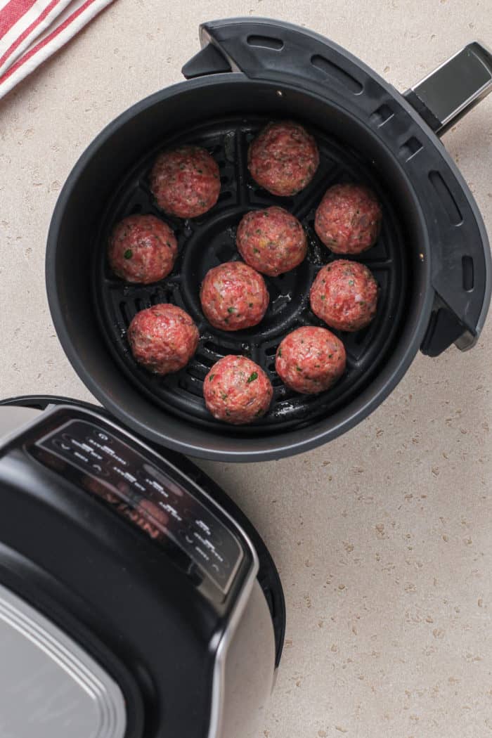 Several rolled meatballs in the basket of an air fryer, ready to be cooked.