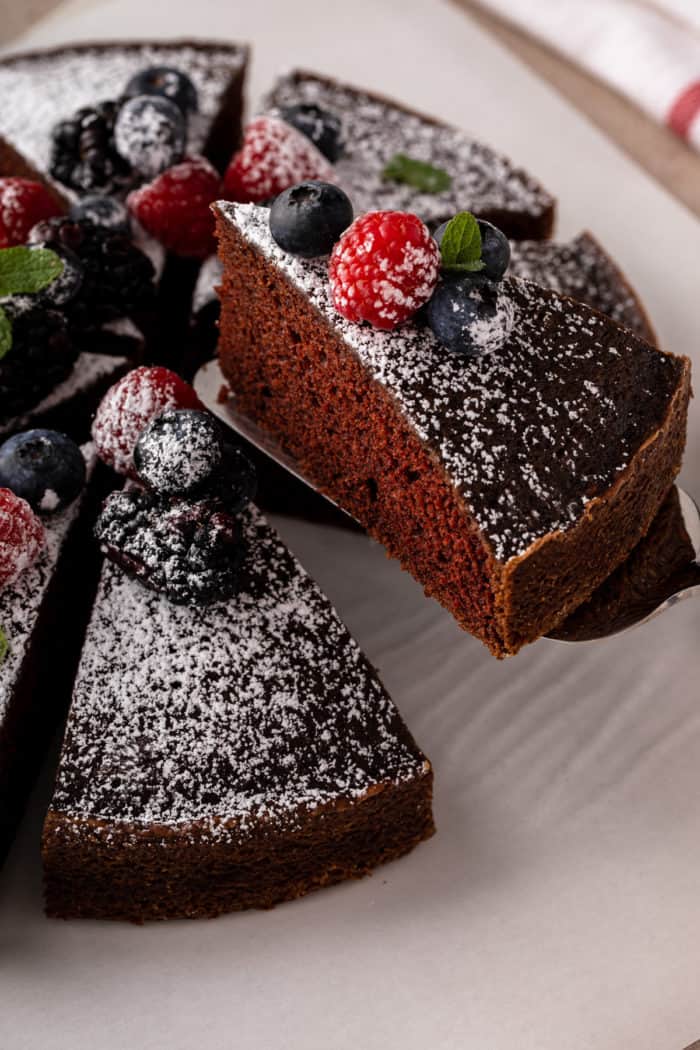 Cake server lifting a slice of eggless chocolate cake off of a cake plate.