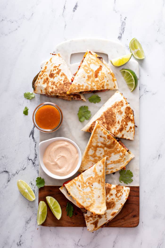 Overhead view of sliced chipotle quesadillas arranged on a marble board with a bowl of dipping sauce.