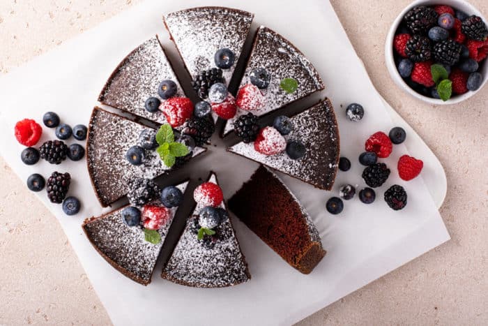 Overhead view of a sliced eggless chocolate cake, topped with fresh berries and a dusting of powdered sugar.