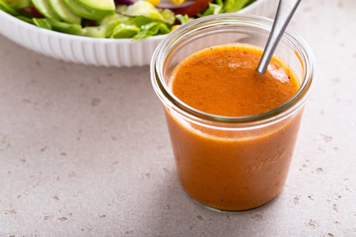 Jar of chipotle vinaigrette on a gray countertop. A spoon is in the jar of dressing.
