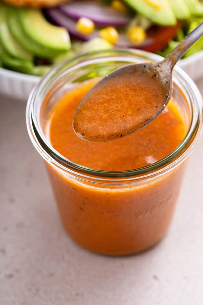 Spoonful of chipotle vinaigrette being held above a jar of the dressing.