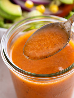 Spoon holding up a spoonful of chipotle vinaigrette over a jar of the dressing.