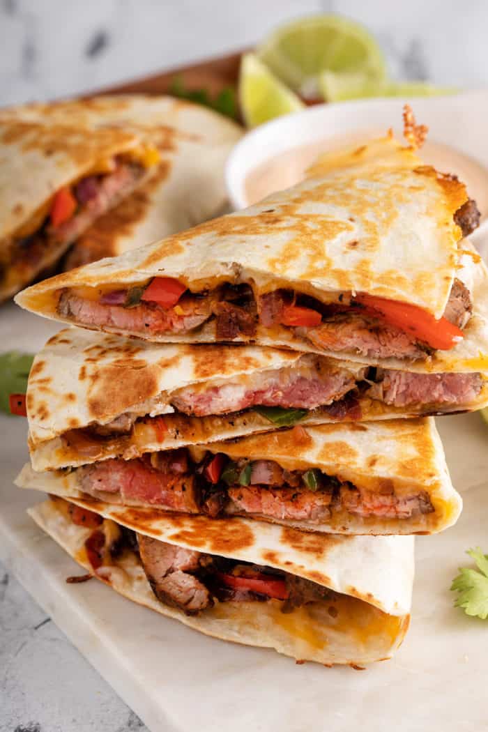 Several slices of chipotle quesadilla stacked on top of each other, with a small bowl of dipping sauce visible in the background.