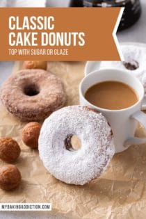 Powdered-sugar-coated cake donut propped up next to a cup of coffee. More cake donuts and donut holes are visible in the background. Text overlay includes recipe name.