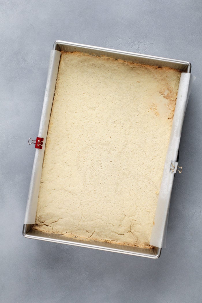 Baked shortbread crust for coconut cream bars in a lined metal baking pan.