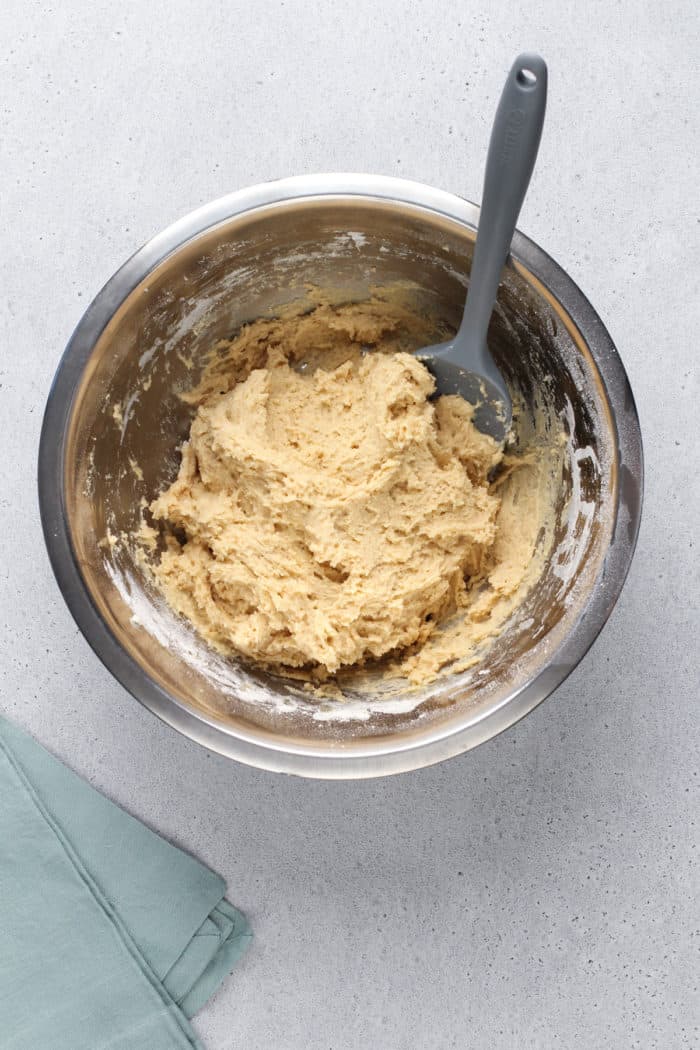 Cake donut dough being stirred in a metal mixing bowl.