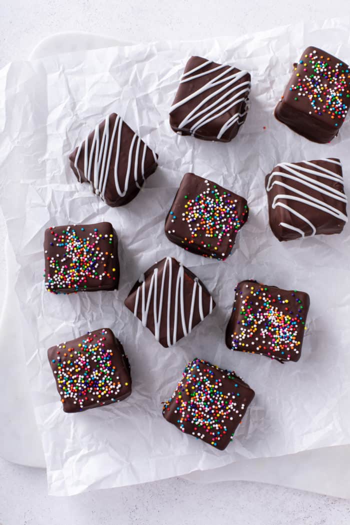 Overhead view of several chocolate-covered homemade marshmallows decorated with white chocolate drizzles and colorful sprinkles.