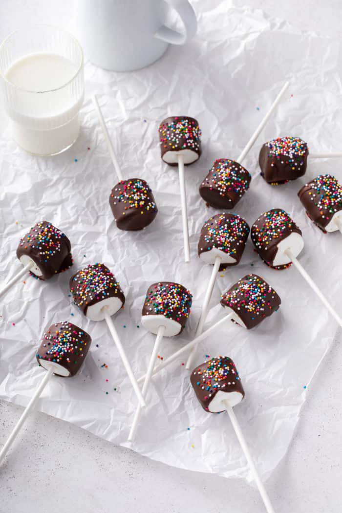 Chocolate-covered marshmallows on cake pop sticks set on a piece of parchment paper.