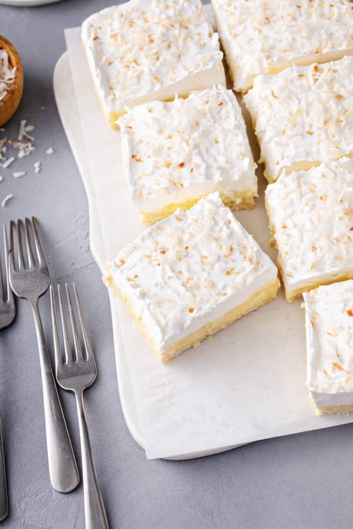 Slices of coconut cream bars on a white parchment-lined platter.
