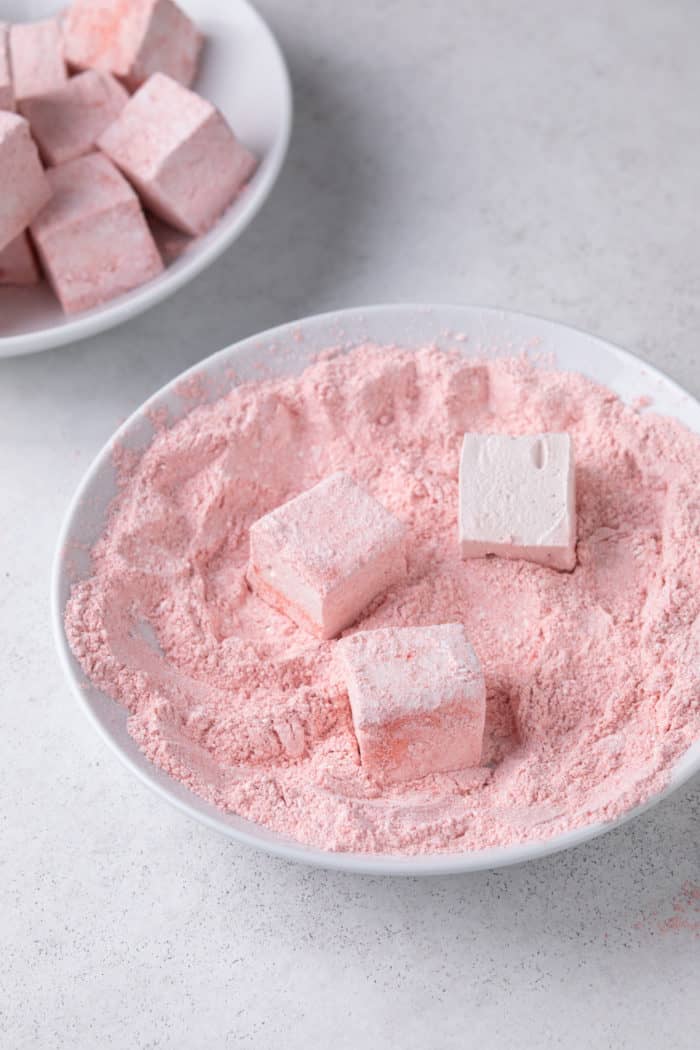 Cut strawberry marshmallows being dredged in strawberry powder and cornstarch.