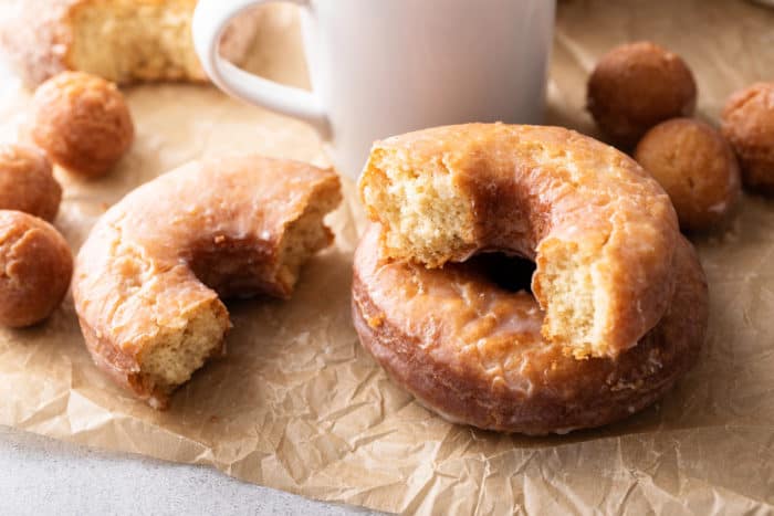 Two cake donuts, one of them broken in half, set next to a white coffee mug.
