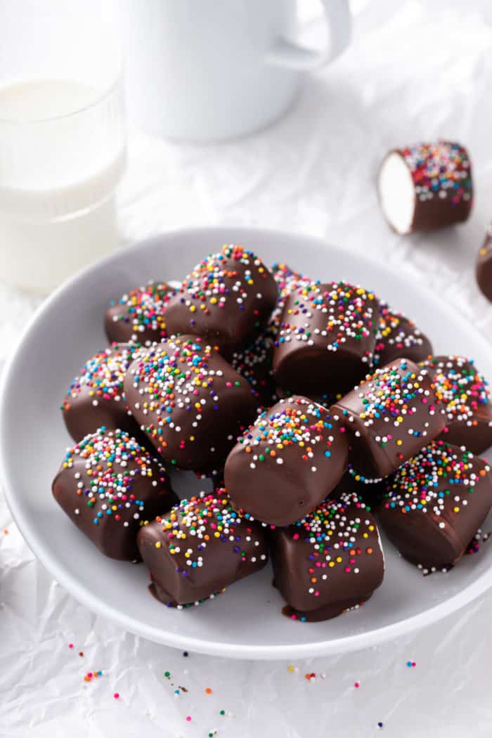 Chocolate-covered marshmallows decorated with rainbow sprinkles on a white plate.