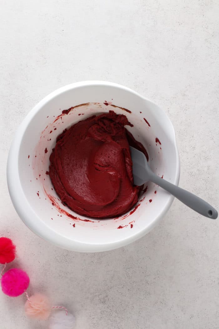Red velvet crinkle cookie dough in a white mixing bowl, being stirred with a gray spatula.