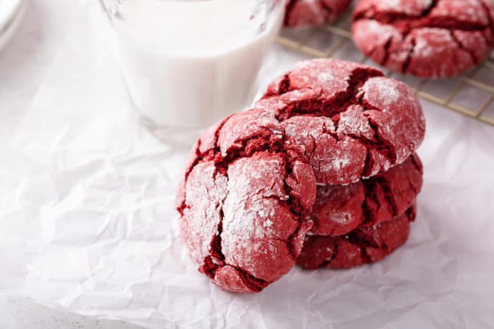 Three stacked crinkle cookies in front of a glass of milk. A fourth crinkle cookie is leaning against the stack.