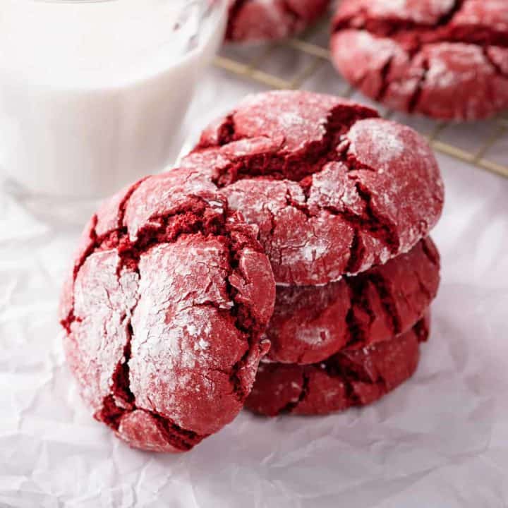 Three stacked red velvet crinkle cookies with a fourth cookie leaning against the stack.