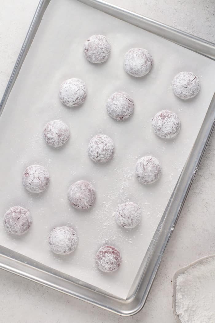 Unbaked red velvet crinkle cookies on a parchment-lined baking sheet, ready to go in the oven.
