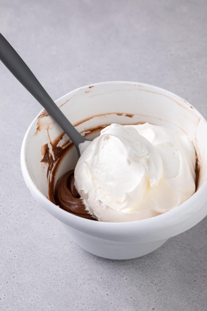 Thawed cool whip being added to a white mixing bowl of nutella fruit dip.