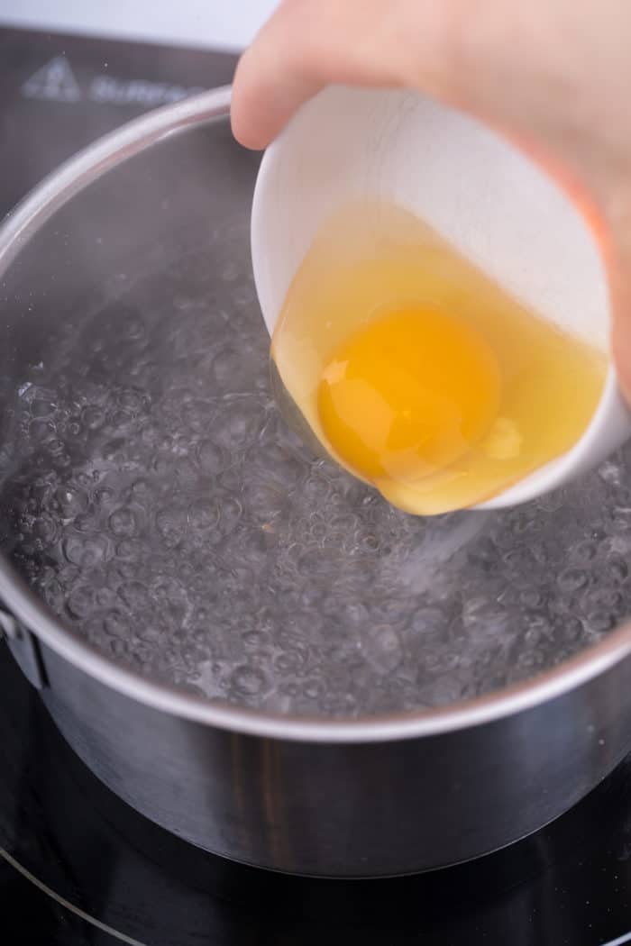 Egg being lowered into simmering water for poaching.