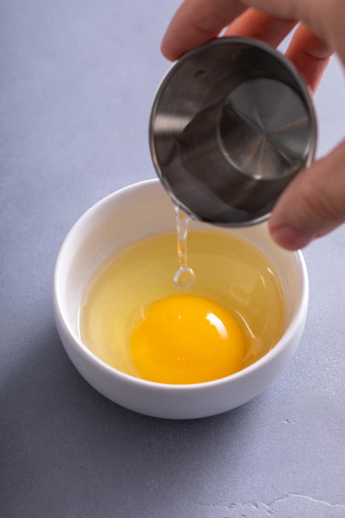 Adding vinegar to a cracked egg in a ramekin.