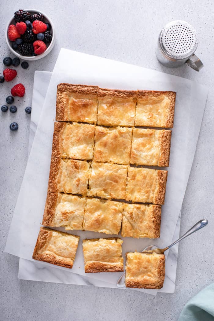 Overhead view of baked and sliced gooey butter cake on a piece of parchment paper.