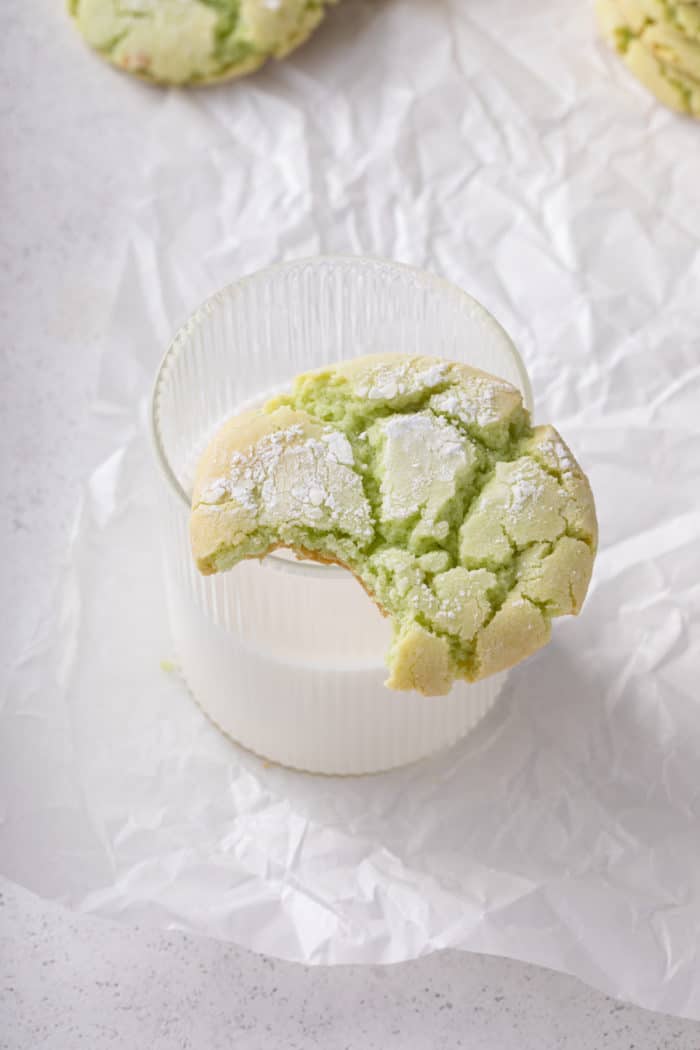 Bite taken from a st. patrick's day crinkle cookie. The cookie is balanced on the edge of a glass of milk.