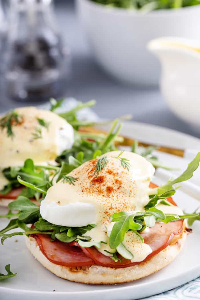 Eggs benedict with canadian bacon and arugula on a white plate.