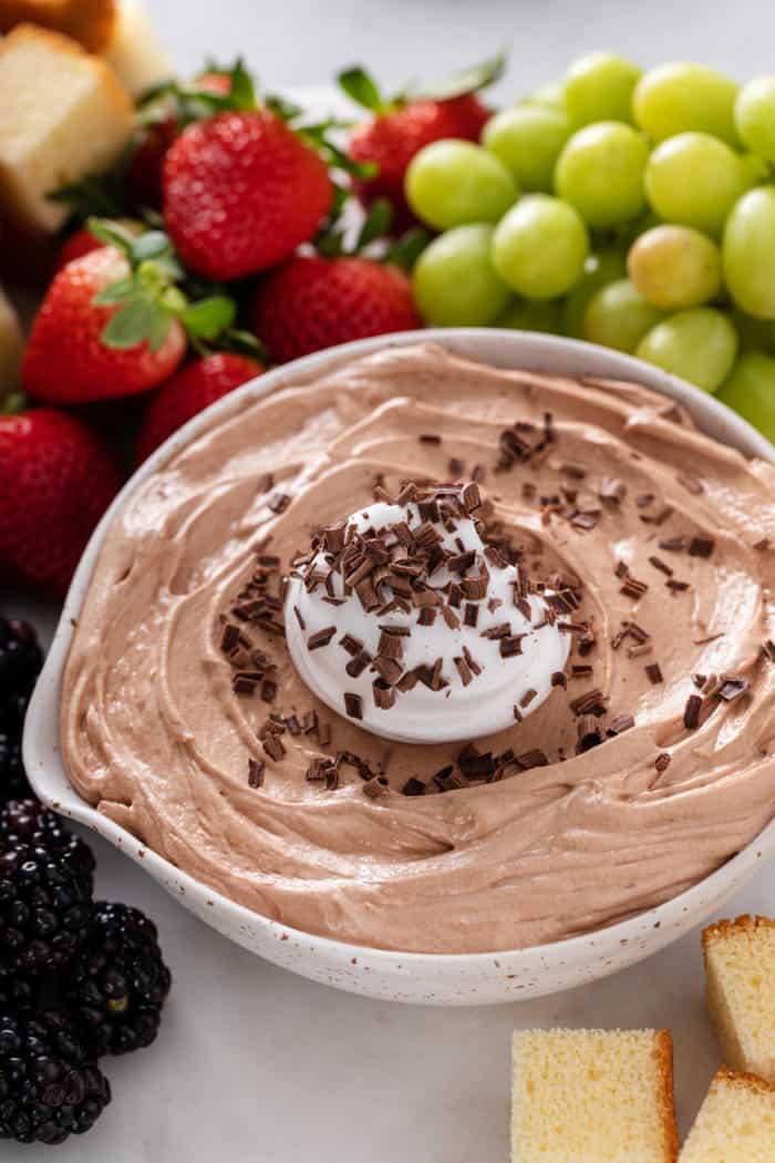 Close up of nutella fruit dip in a white serving bowl, topped with whipped cream and chocolate shavings.