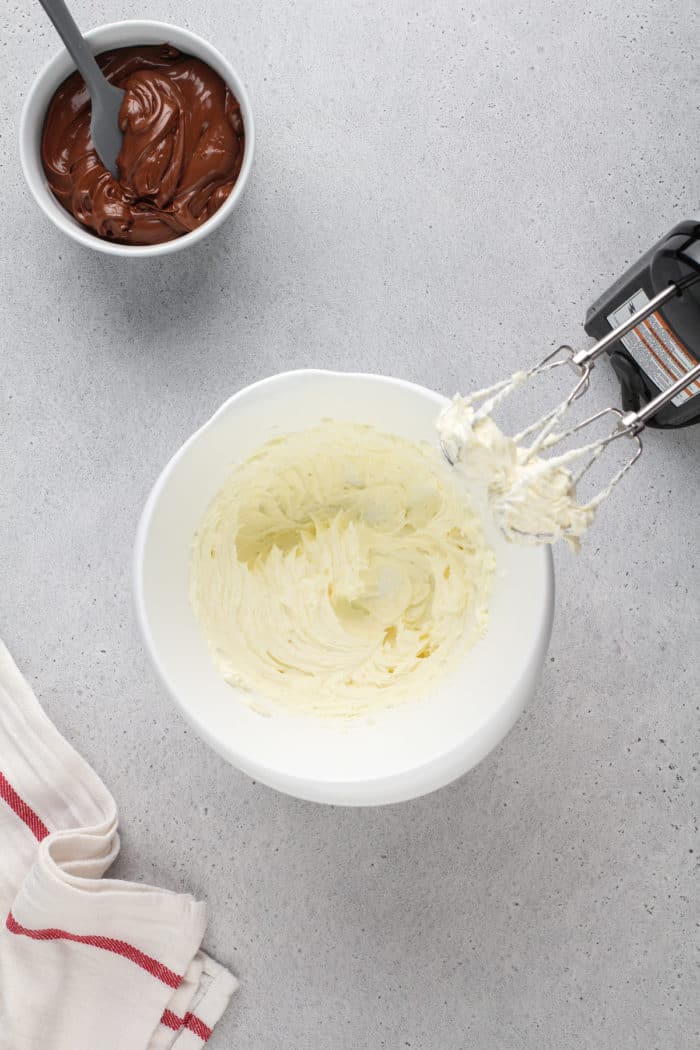 Cream cheese and powdered sugar beaten together in a white mixing bowl for fruit dip.