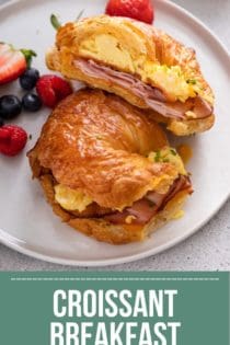 White plate topped with a halved croissant breakfast sandwich and fresh berries. Text overlay includes recipe name.