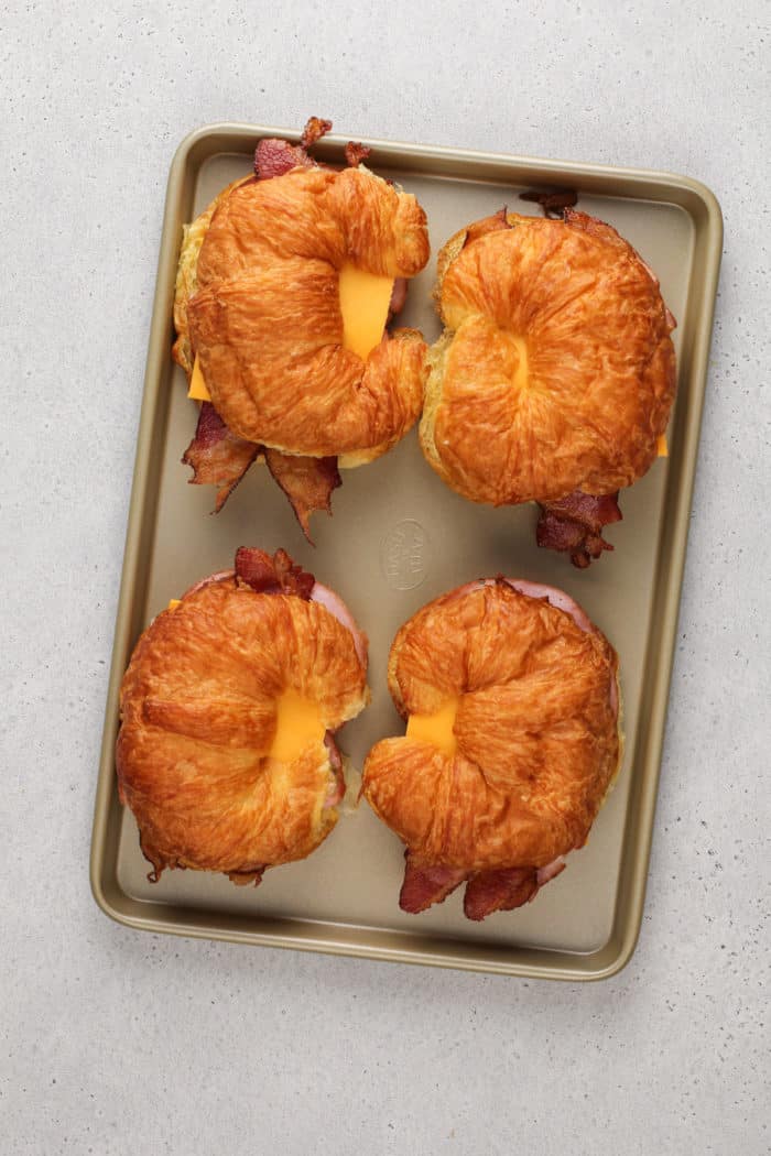Assembled croissant breakfast sandwiches on a sheet pan, ready to go in the oven.