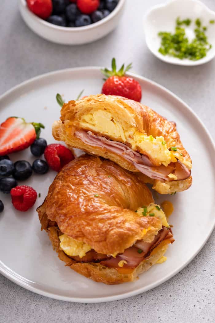 White plate topped with a halved croissant breakfast sandwich and fresh berries.
