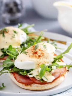 Eggs benedict with canadian bacon and arugula on a white plate.