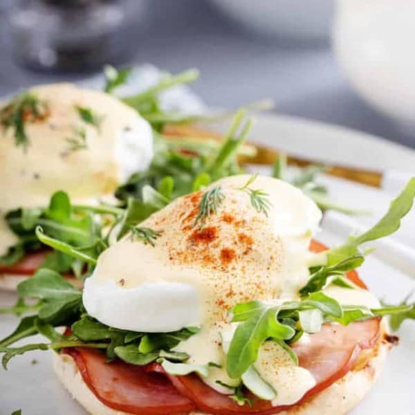 Eggs benedict with canadian bacon and arugula on a white plate.