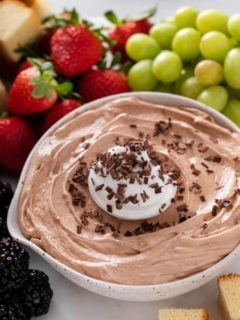 Close up of nutella fruit dip in a white serving bowl, topped with whipped cream and chocolate shavings.