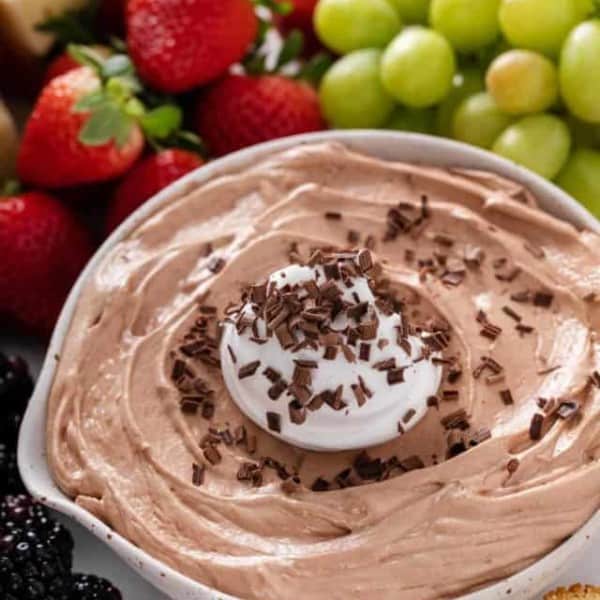 Close up of nutella fruit dip in a white serving bowl, topped with whipped cream and chocolate shavings.