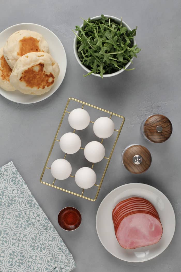 Components for eggs benedict arranged on a gray countertop.