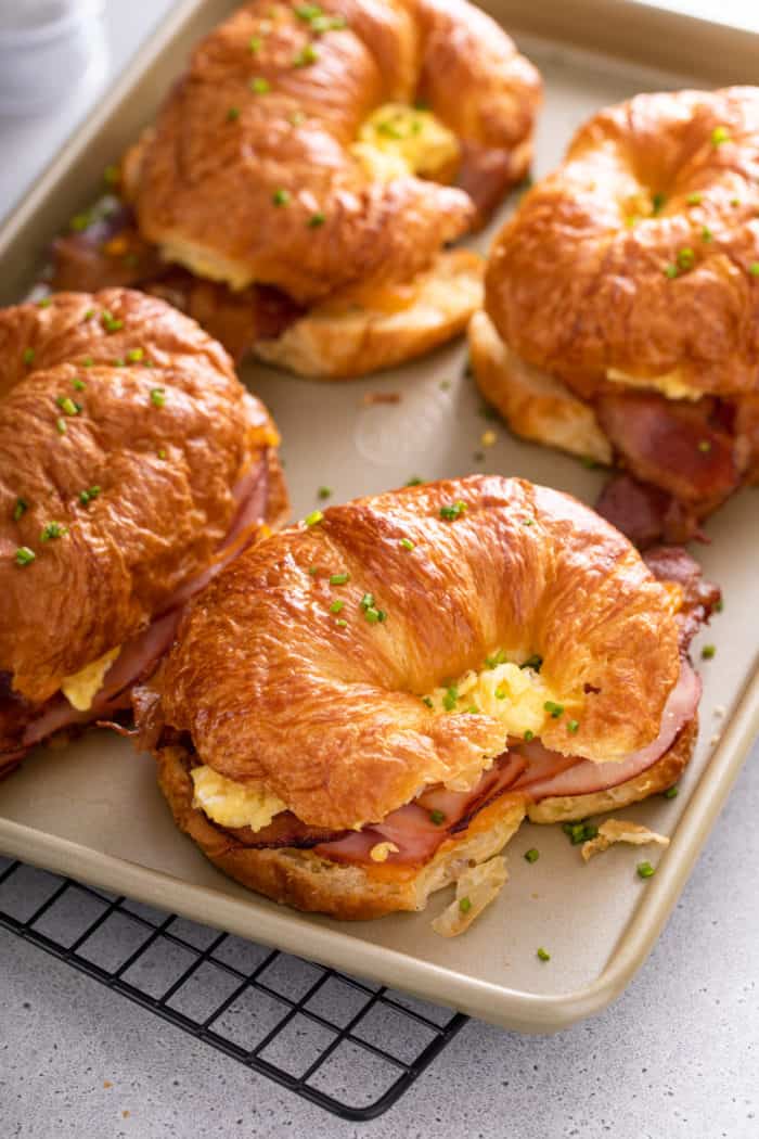 Assembled and baked croissant breakfast sandwiches on a sheet pan, topped with fresh chives.