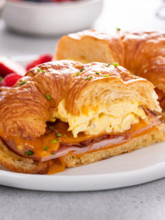 Halved croissant breakfast sandwich on a white plate.