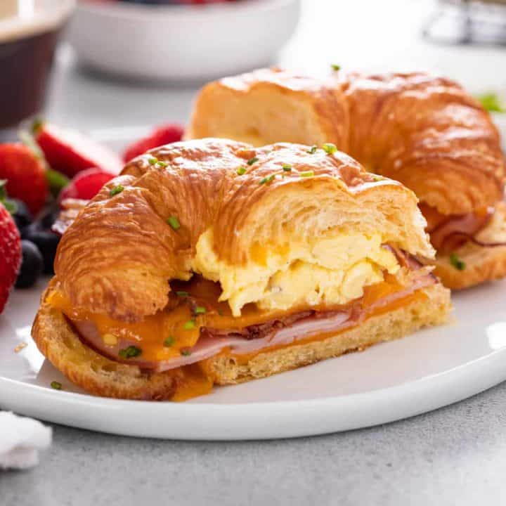 Halved croissant breakfast sandwich on a white plate.