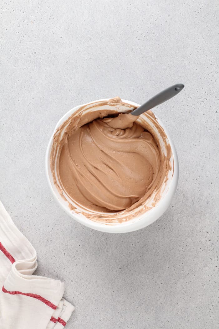 Nutella fruit dip folded together with a spatula in a white mixing bowl.