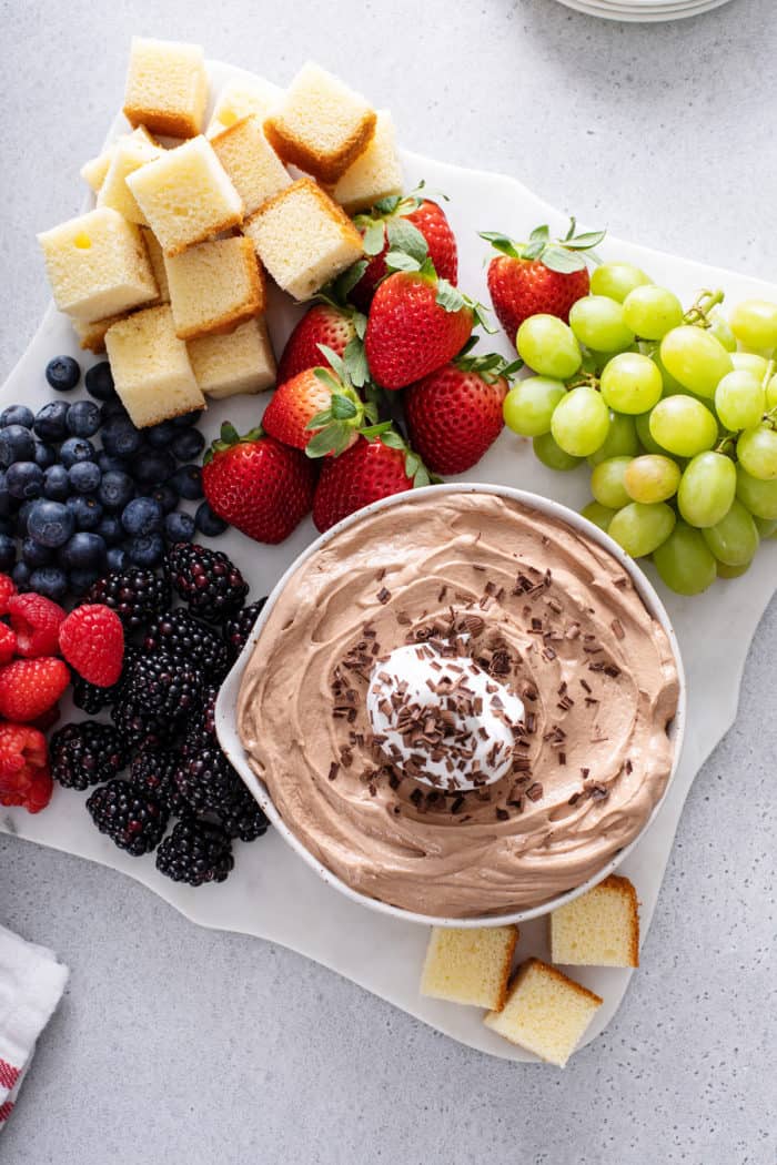 Overhead view of nutella fruit dip in a white bowl set on a platter next to fresh fruit and cubes of pound cake.