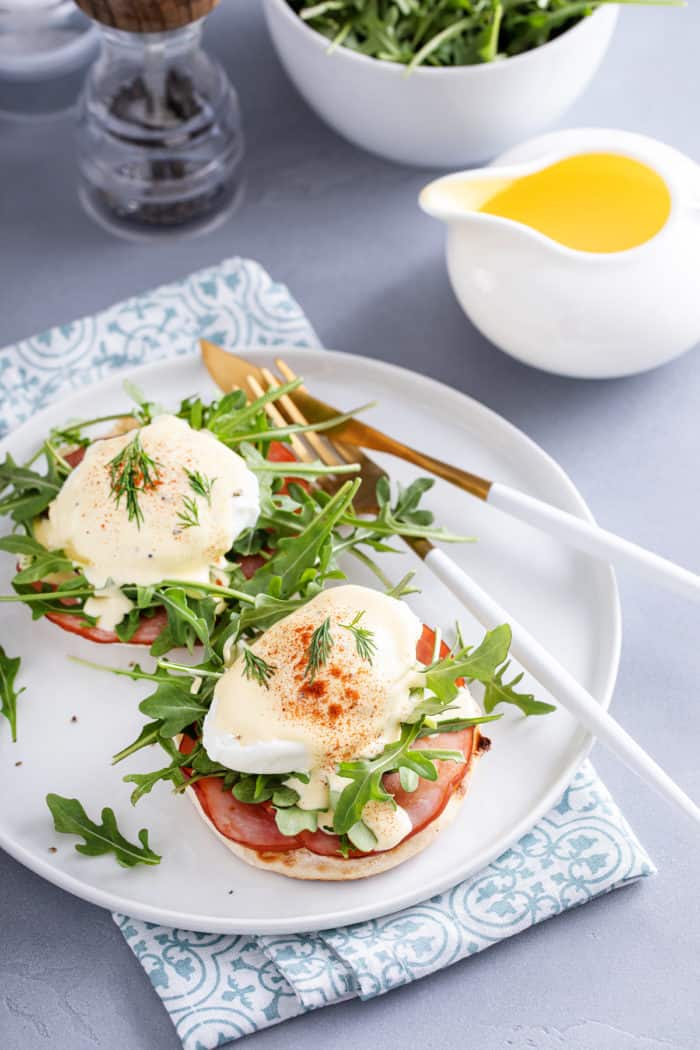 White plate with eggs benedict set next to a container of hollandaise.